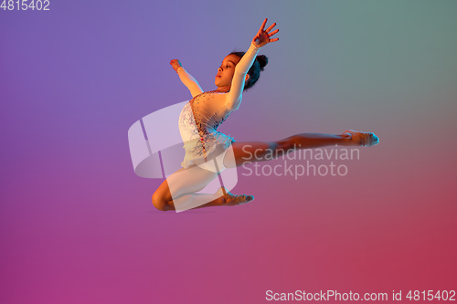 Image of African-american rhythmic gymnast, pretty girl practicing on gradient studio background in neon light