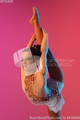 Image of African-american rhythmic gymnast, pretty girl practicing on gradient studio background in neon light