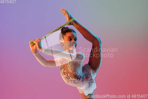 Image of African-american rhythmic gymnast, pretty girl practicing on gradient studio background in neon light