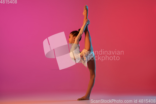 Image of African-american rhythmic gymnast, pretty girl practicing on gradient studio background in neon light