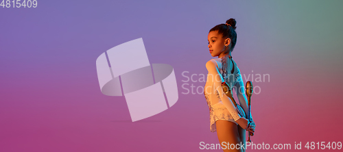 Image of African-american rhythmic gymnast, pretty girl practicing on gradient studio background in neon light