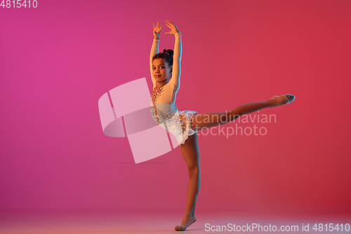 Image of African-american rhythmic gymnast, pretty girl practicing on gradient studio background in neon light