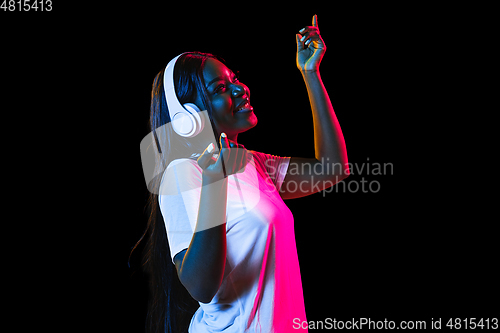 Image of African young woman\'s portrait on dark studio background in neon. Concept of human emotions, facial expression, youth, sales, ad.