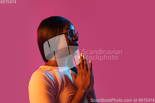 Image of African young woman\'s portrait on pink studio background in neon. Concept of human emotions, facial expression, youth, sales, ad.