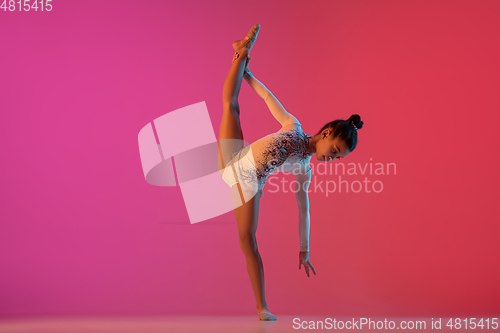 Image of African-american rhythmic gymnast, pretty girl practicing on gradient studio background in neon light