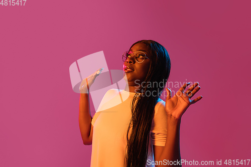 Image of African young woman\'s portrait on pink studio background in neon. Concept of human emotions, facial expression, youth, sales, ad.