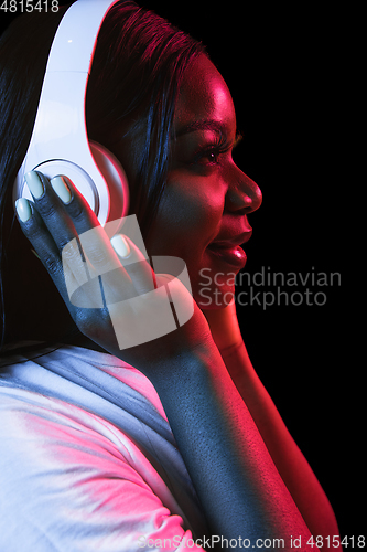 Image of African young woman\'s portrait on dark studio background in neon. Concept of human emotions, facial expression, youth, sales, ad.