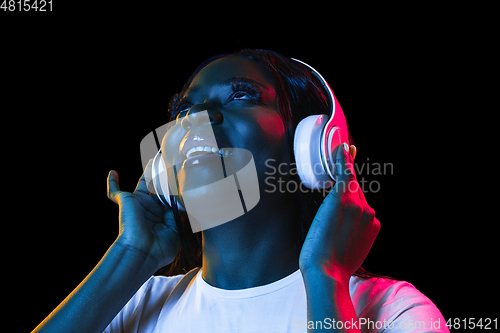 Image of African young woman\'s portrait on dark studio background in neon. Concept of human emotions, facial expression, youth, sales, ad.