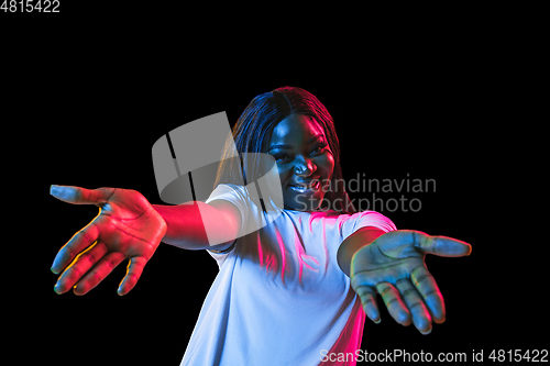 Image of African young woman\'s portrait on dark studio background in neon. Concept of human emotions, facial expression, youth, sales, ad.