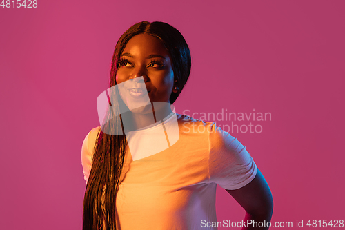 Image of African young woman\'s portrait on pink studio background in neon. Concept of human emotions, facial expression, youth, sales, ad.