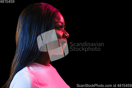 Image of African young woman\'s portrait on dark studio background in neon. Concept of human emotions, facial expression, youth, sales, ad.