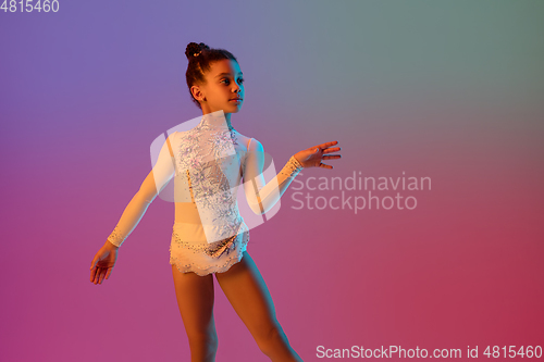 Image of African-american rhythmic gymnast, pretty girl practicing on gradient studio background in neon light