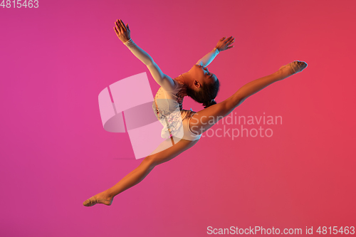 Image of African-american rhythmic gymnast, pretty girl practicing on gradient studio background in neon light