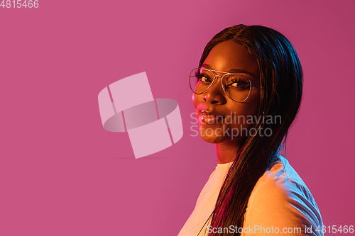 Image of African young woman\'s portrait on pink studio background in neon. Concept of human emotions, facial expression, youth, sales, ad.