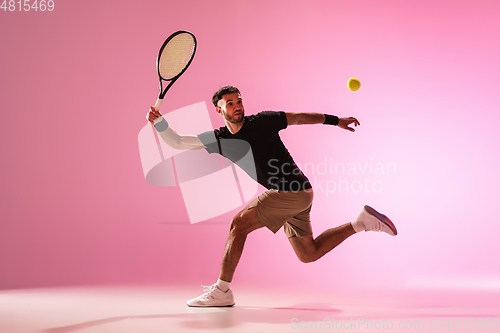 Image of Young caucasian man playing tennis isolated on pink studio background, action and motion concept