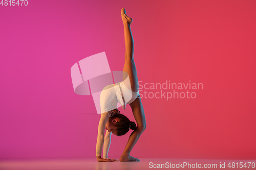 Image of African-american rhythmic gymnast, pretty girl practicing on gradient studio background in neon light