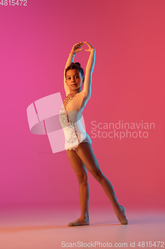 Image of African-american rhythmic gymnast, pretty girl practicing on gradient studio background in neon light