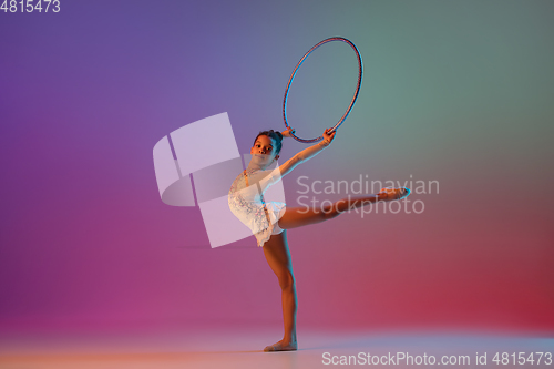 Image of African-american rhythmic gymnast, pretty girl practicing on gradient studio background in neon light