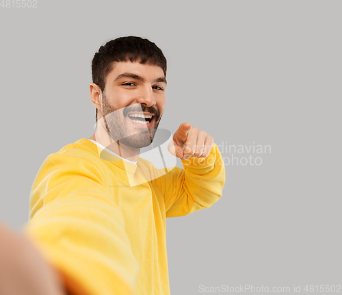 Image of happy young man in yellow sweatshirt making selfie