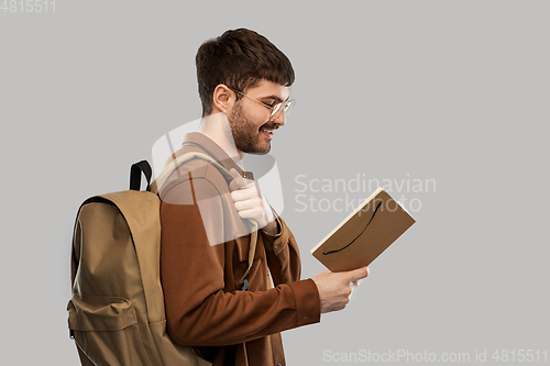 Image of smiling young man with backpack reading diary