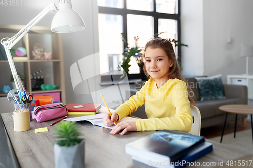 Image of student girl with book writing to notebook at home