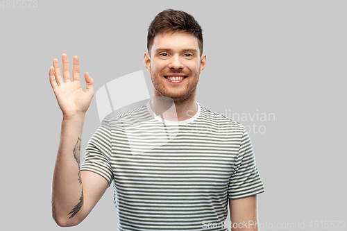 Image of smiling young man in striped t-shirt waving hand