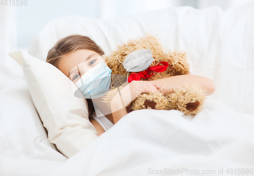 Image of girl wearing medical mask with teddy bear in bed