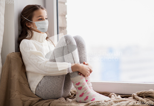 Image of sad girl in medical mask sitting on sill at home