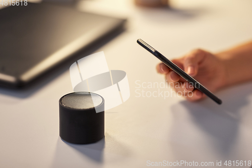 Image of hand with smartphone and smart speaker at office