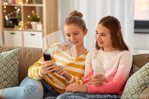 Image of happy teenage girls with smartphones at home