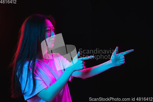 Image of Asian young woman\'s portrait on dark studio background in neon. Concept of human emotions, facial expression, youth, sales, ad.