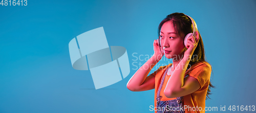 Image of Asian young woman\'s portrait on blue studio background in neon. Concept of human emotions, facial expression, youth, sales, ad.