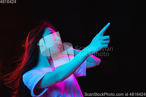 Image of Asian young woman\'s portrait on dark studio background in neon. Concept of human emotions, facial expression, youth, sales, ad.