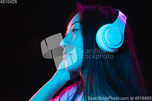 Image of Asian young woman\'s portrait on dark studio background in neon. Concept of human emotions, facial expression, youth, sales, ad.