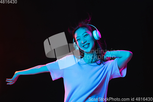 Image of Asian young woman\'s portrait on dark studio background in neon. Concept of human emotions, facial expression, youth, sales, ad.