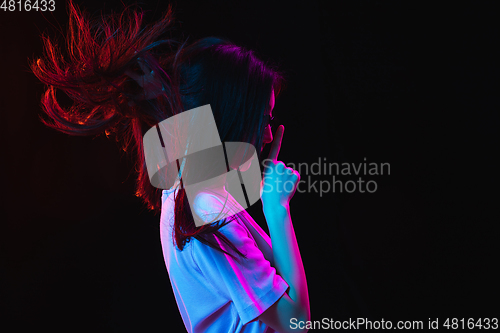 Image of Asian young woman\'s portrait on dark studio background in neon. Concept of human emotions, facial expression, youth, sales, ad.