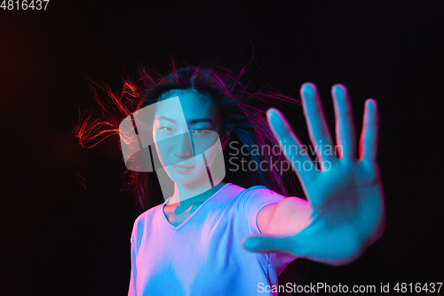 Image of Asian young woman\'s portrait on dark studio background in neon. Concept of human emotions, facial expression, youth, sales, ad.