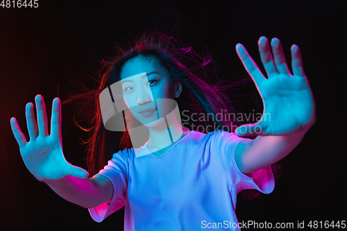 Image of Asian young woman\'s portrait on dark studio background in neon. Concept of human emotions, facial expression, youth, sales, ad.