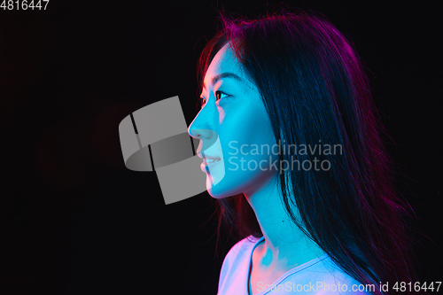 Image of Asian young woman\'s portrait on dark studio background in neon. Concept of human emotions, facial expression, youth, sales, ad.