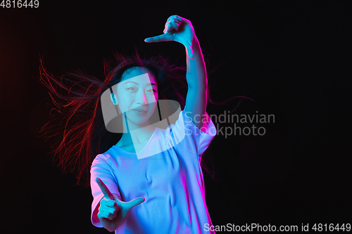 Image of Asian young woman\'s portrait on dark studio background in neon. Concept of human emotions, facial expression, youth, sales, ad.