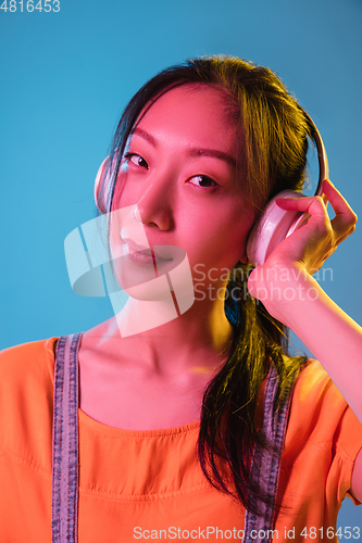 Image of Asian young woman\'s portrait on blue studio background in neon. Concept of human emotions, facial expression, youth, sales, ad.