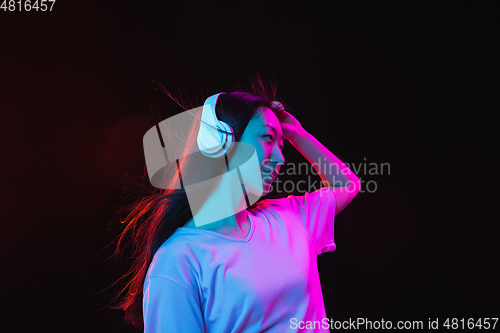 Image of Asian young woman\'s portrait on dark studio background in neon. Concept of human emotions, facial expression, youth, sales, ad.