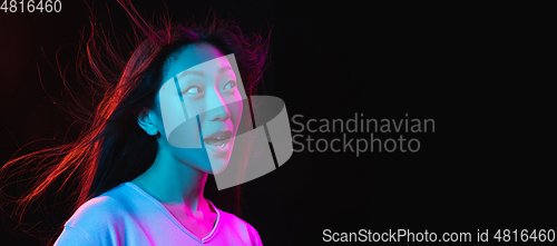 Image of Asian young woman\'s portrait on dark studio background in neon. Concept of human emotions, facial expression, youth, sales, ad.