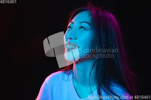 Image of Asian young woman\'s portrait on dark studio background in neon. Concept of human emotions, facial expression, youth, sales, ad.