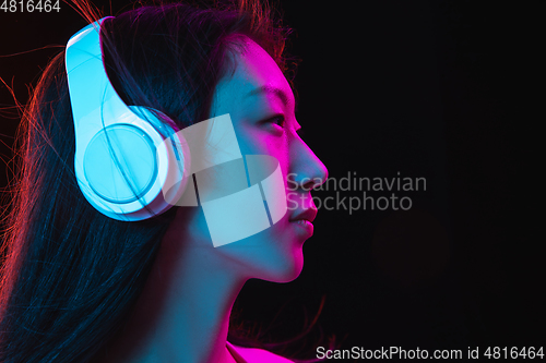 Image of Asian young woman\'s portrait on dark studio background in neon. Concept of human emotions, facial expression, youth, sales, ad.