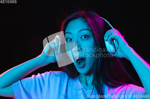 Image of Asian young woman\'s portrait on dark studio background in neon. Concept of human emotions, facial expression, youth, sales, ad.