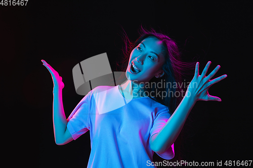 Image of Asian young woman\'s portrait on dark studio background in neon. Concept of human emotions, facial expression, youth, sales, ad.