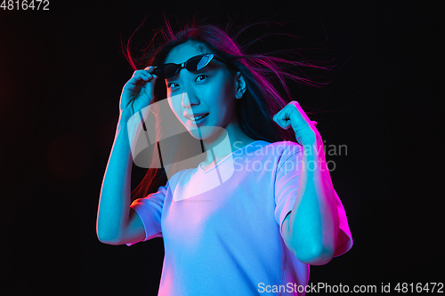 Image of Asian young woman\'s portrait on dark studio background in neon. Concept of human emotions, facial expression, youth, sales, ad.