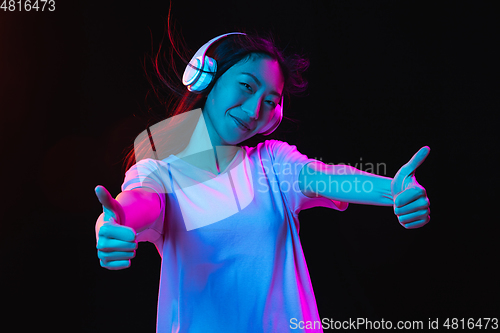 Image of Asian young woman\'s portrait on dark studio background in neon. Concept of human emotions, facial expression, youth, sales, ad.