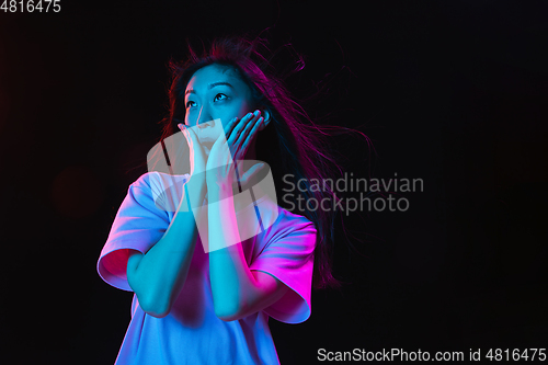 Image of Asian young woman\'s portrait on dark studio background in neon. Concept of human emotions, facial expression, youth, sales, ad.